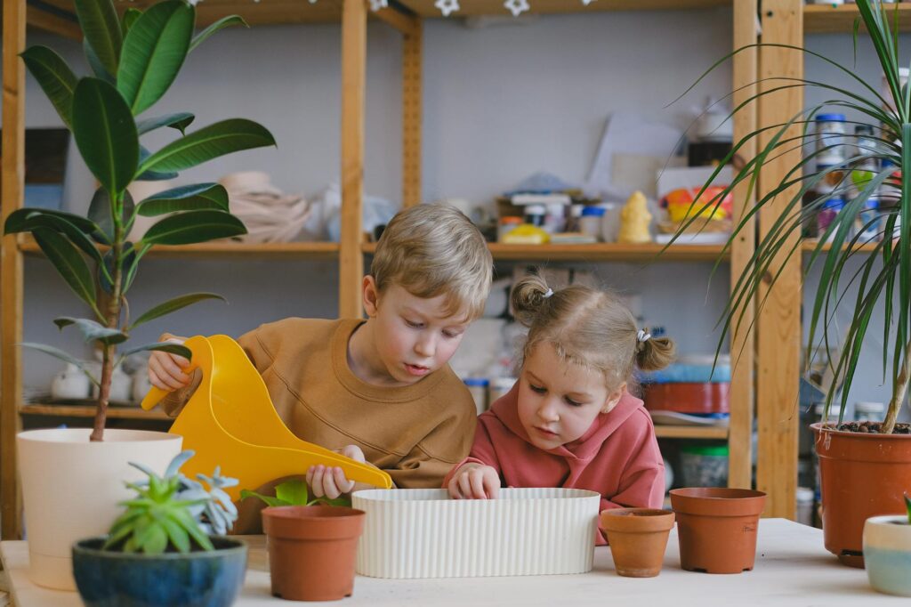Two children indoors, eagerly engaged in gardening and watering plants, sparking curiosity and teamwork.