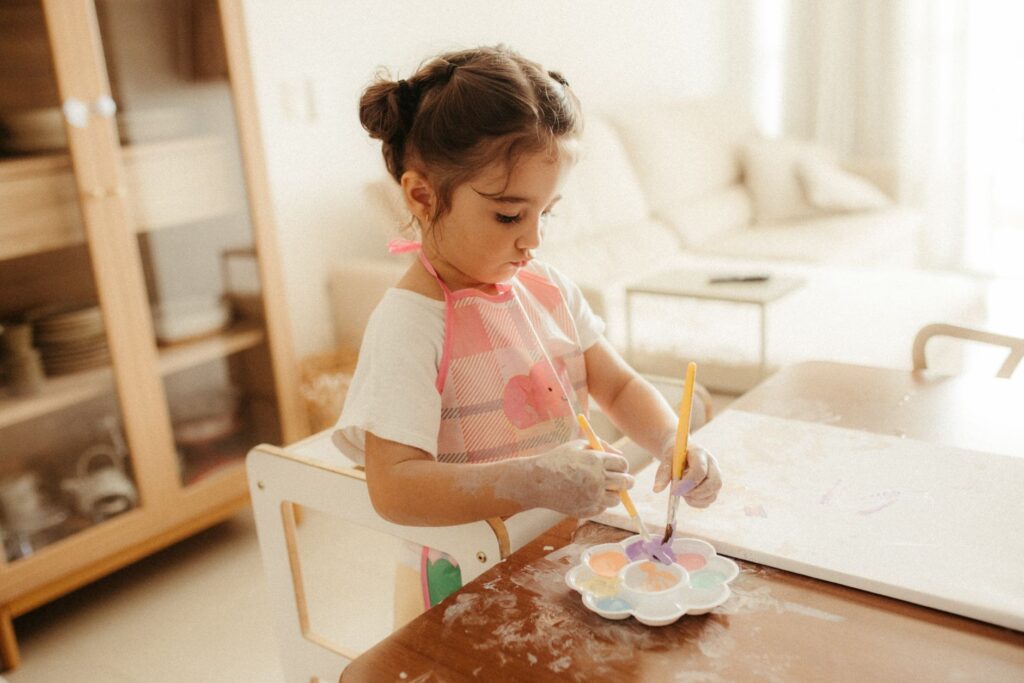 Little girl painting at home with watercolors, fostering creativity and fun indoors.