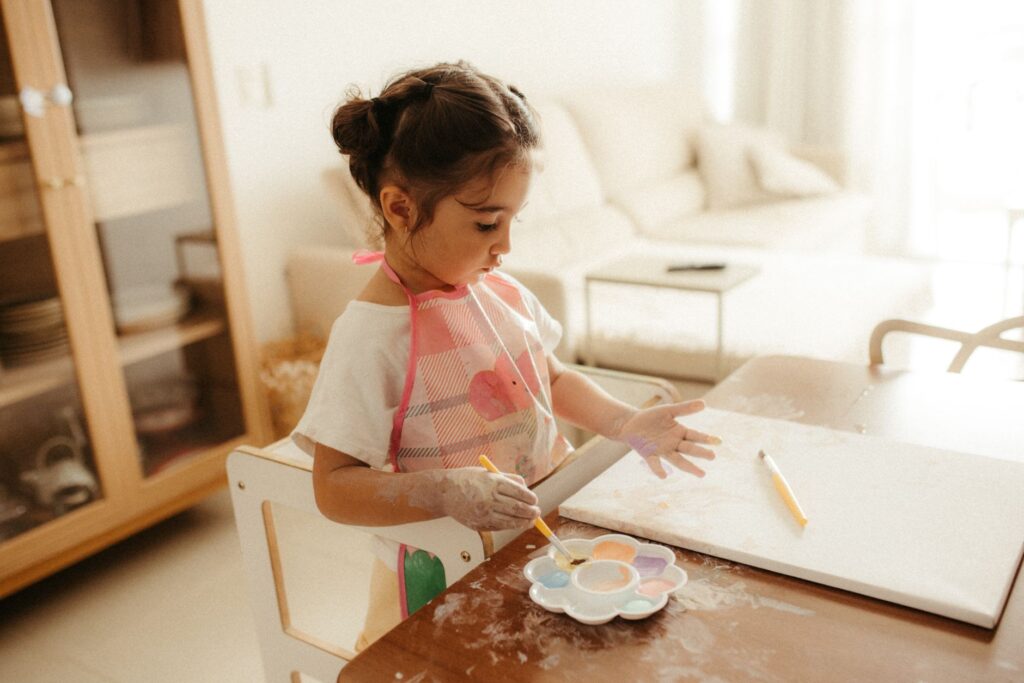 A young girl explores creativity with paints at a home setting, fostering artistic expression.