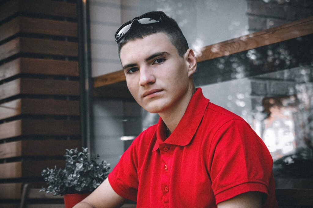 Portrait of a young man wearing a red polo shirt indoors, looking directly at the camera.