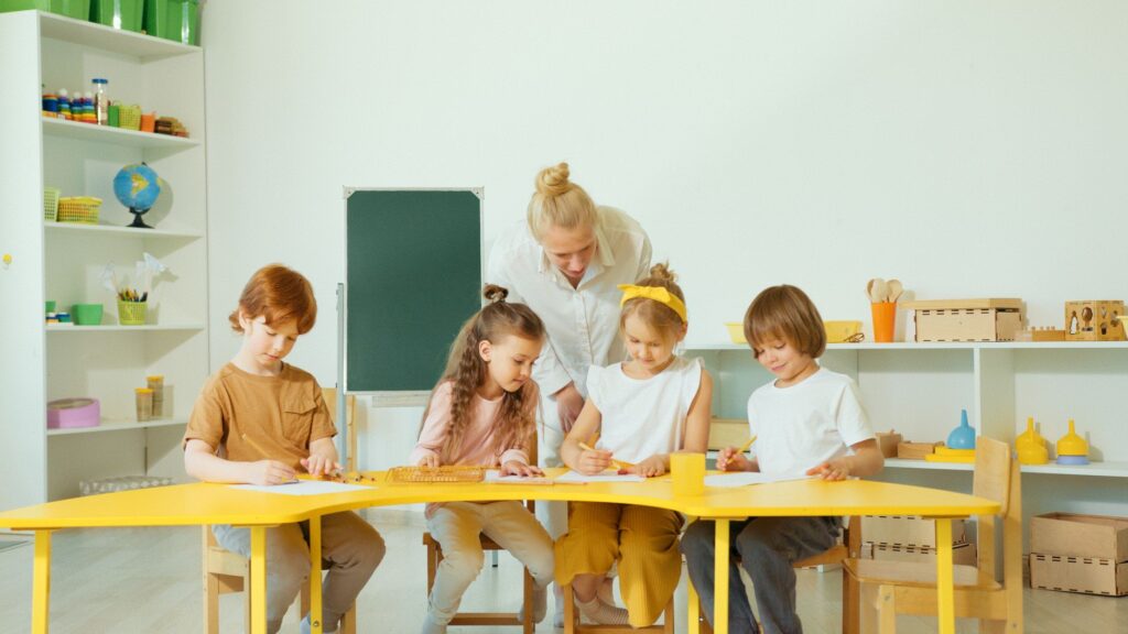 A teacher guides young students in a bright classroom setting.