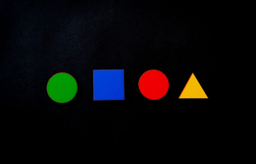 Colorful geometric shapes contrasting against a dark background, featuring circle, square, triangle.