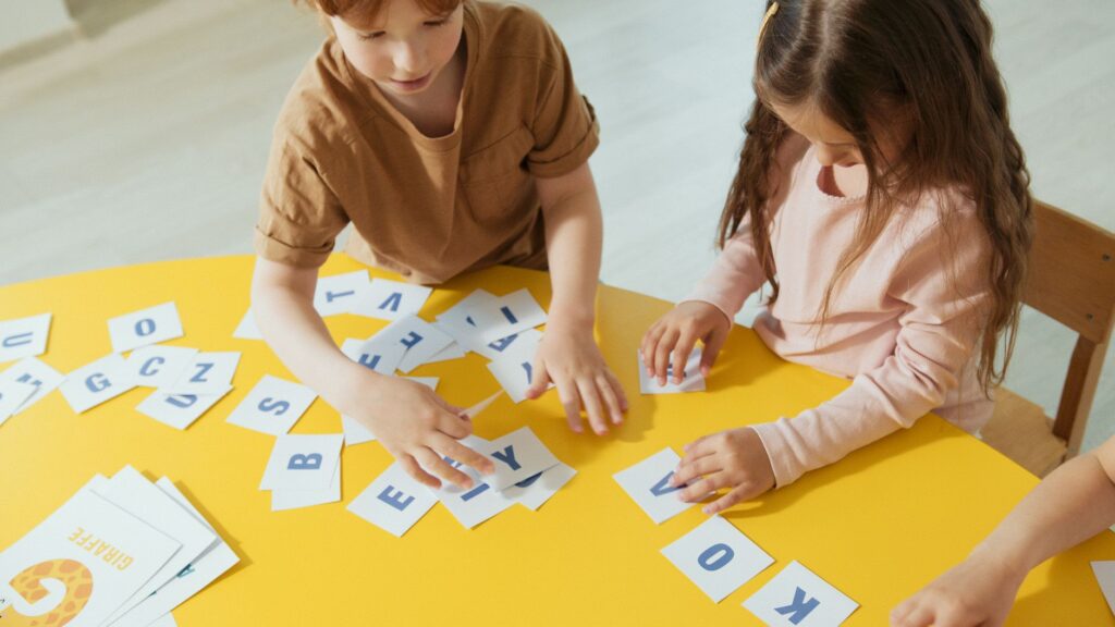 Two children interacting with alphabet cards at a yellow table, enhancing learning and creativity.