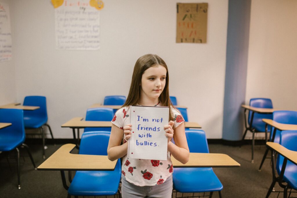 A girl stands in an empty classroom holding an anti-bullying sign.
