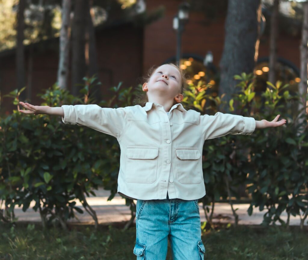 Child embracing nature with open arms in a serene outdoor setting.