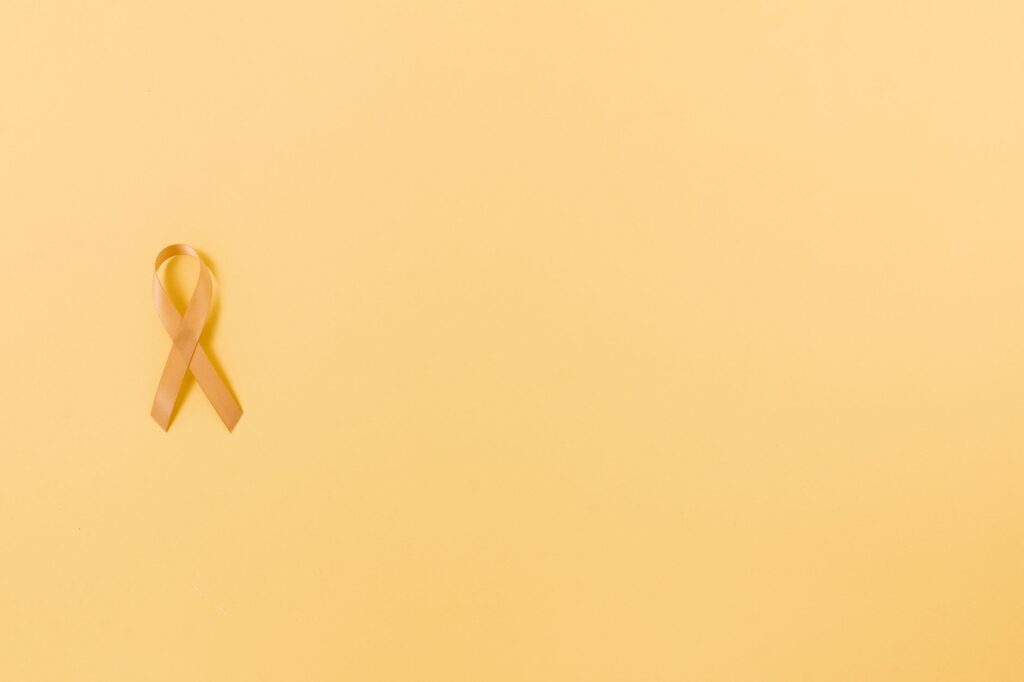 Gold ribbon on a yellow background symbolizing cancer awareness and support.