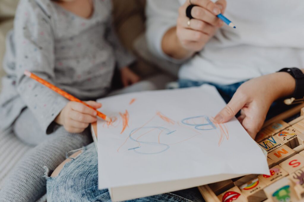 Child and parent drawing together with crayons, expressing creativity and bonding.