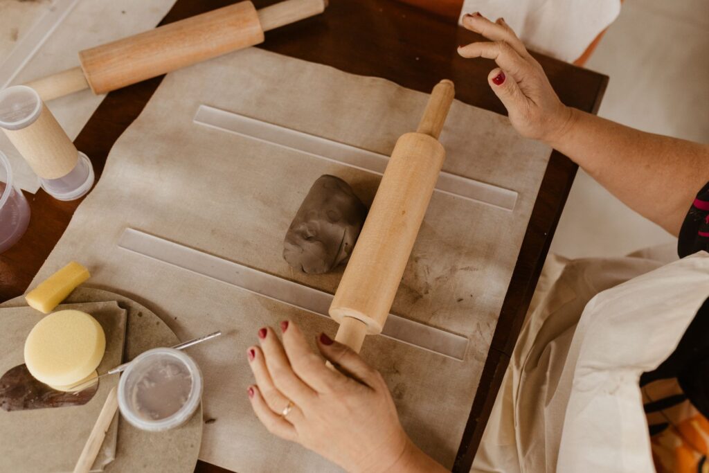 Hands rolling clay with tools and rolling pin on a table, indoors art and craft activity.