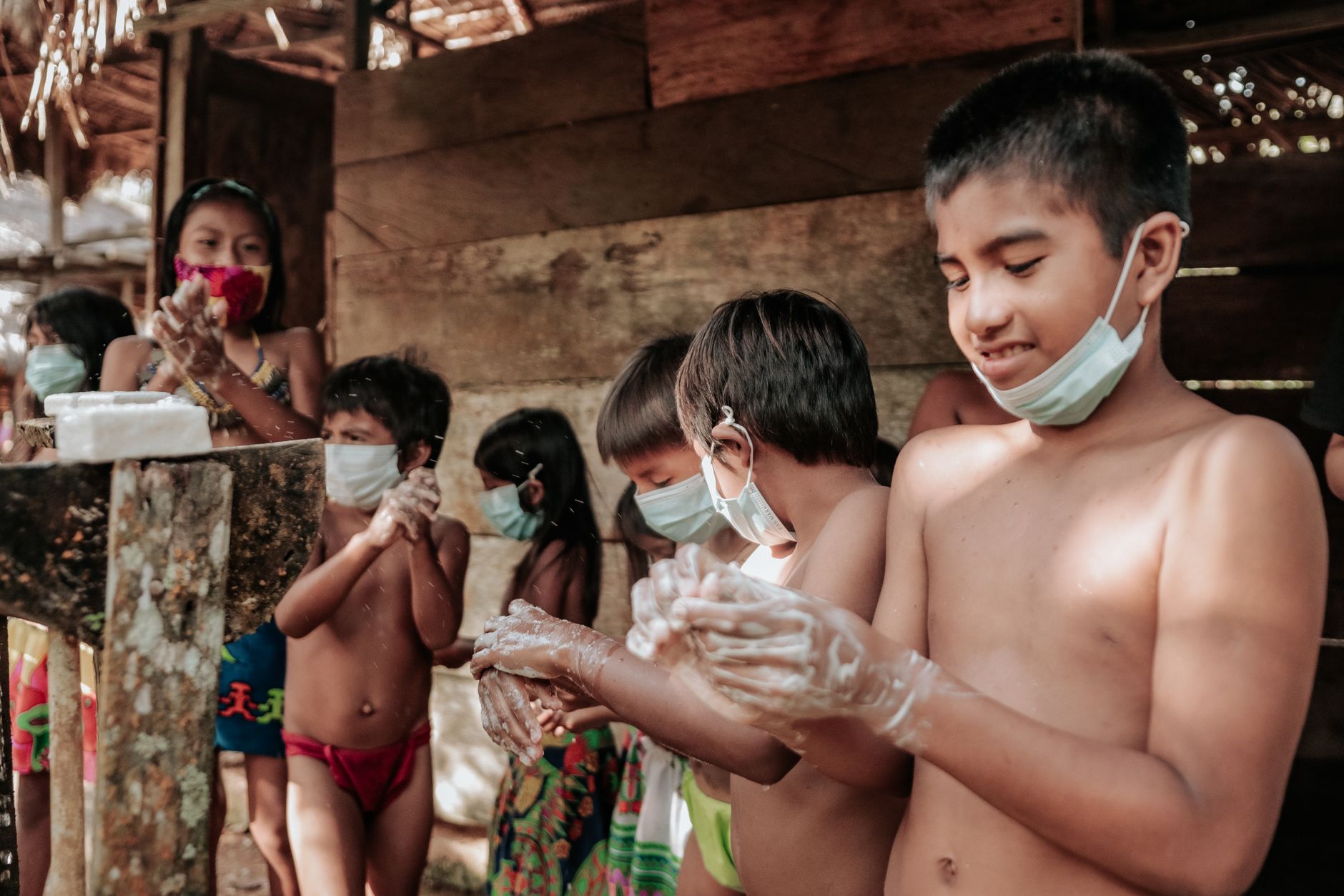 Children in masks washing hands with soap outdoors, promoting hygiene.