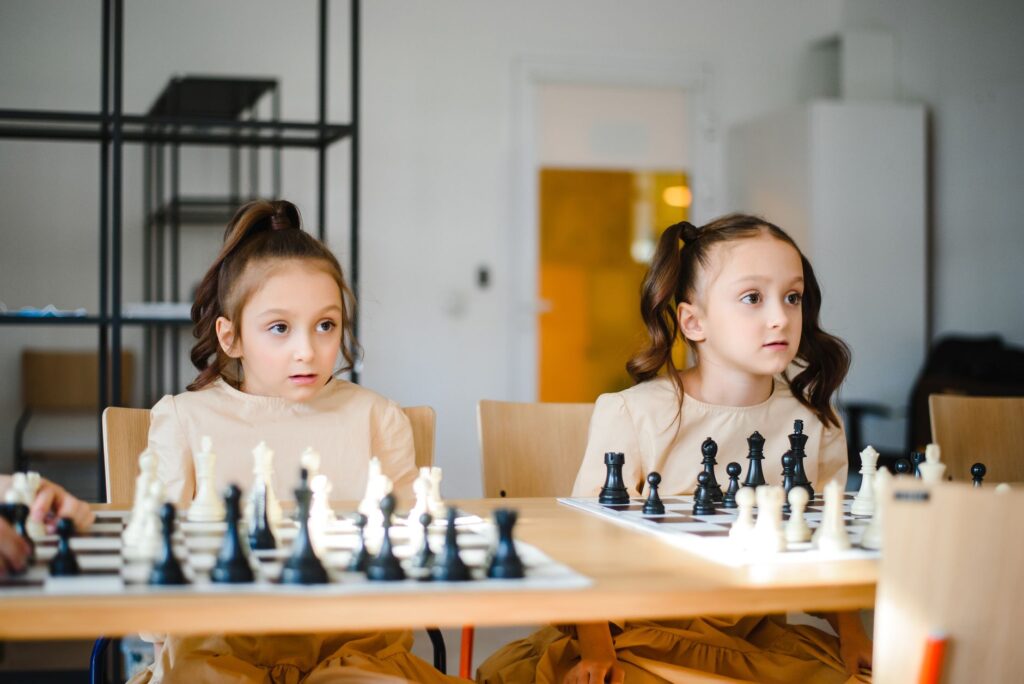 Identical twin sisters playing chess together indoors, focusing on strategy.
