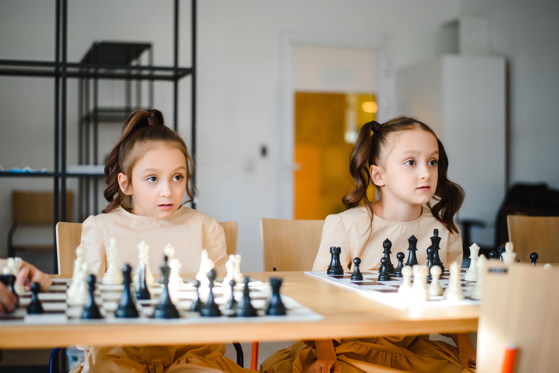 Identical twin sisters playing chess together indoors, focusing on strategy.
