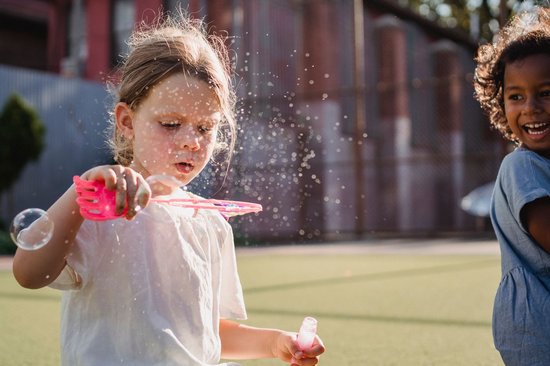 Two kids having fun blowing bubbles in a sunny outdoor playground setting.
