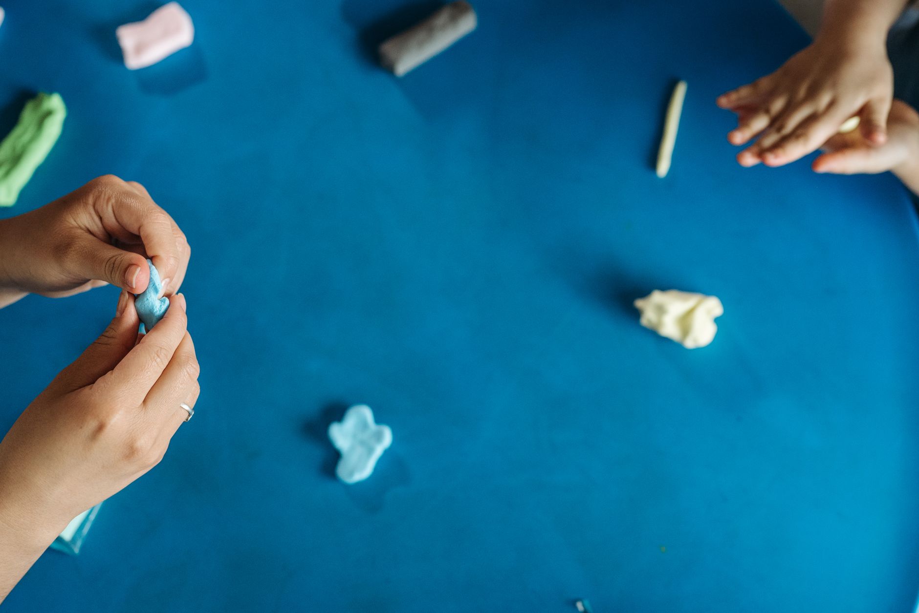 Hands molding colorful clay on a blue table, capturing creativity and play in an artistic process.