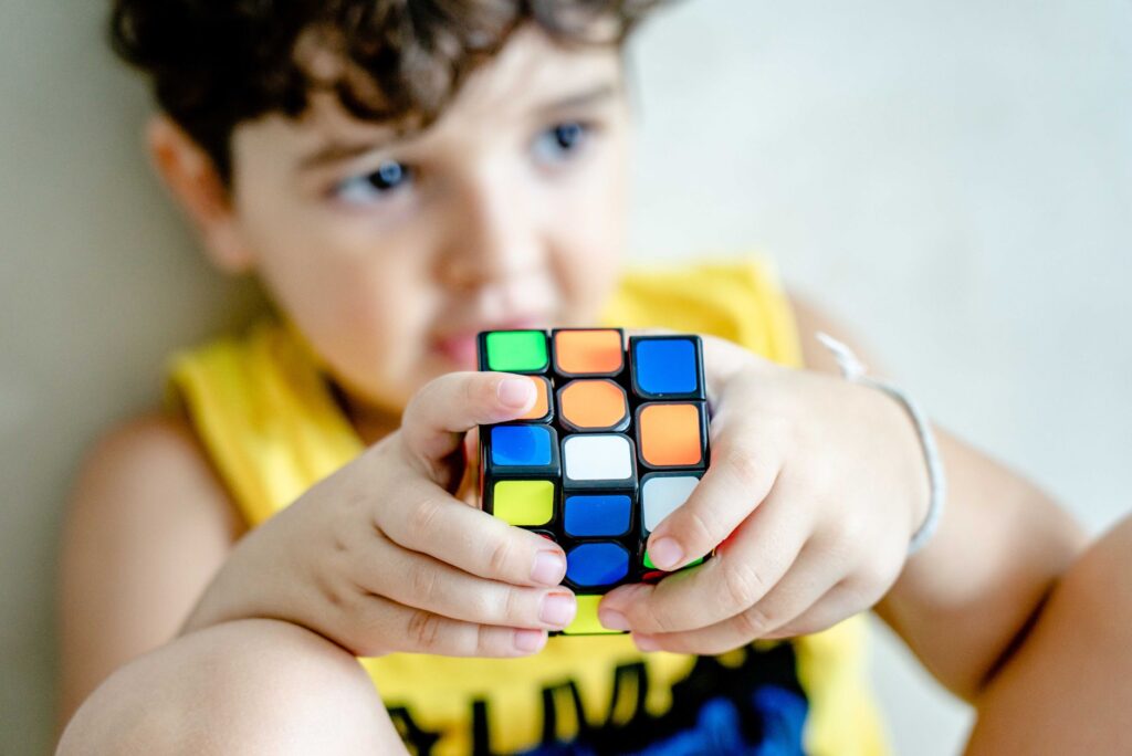 Young boy holding and concentrating on solving a colorful Rubik's Cube indoors.