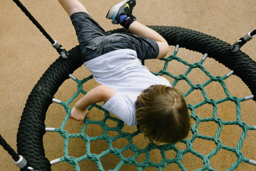 Young boy enjoying a playful moment on a net swing in a sunny park playground.