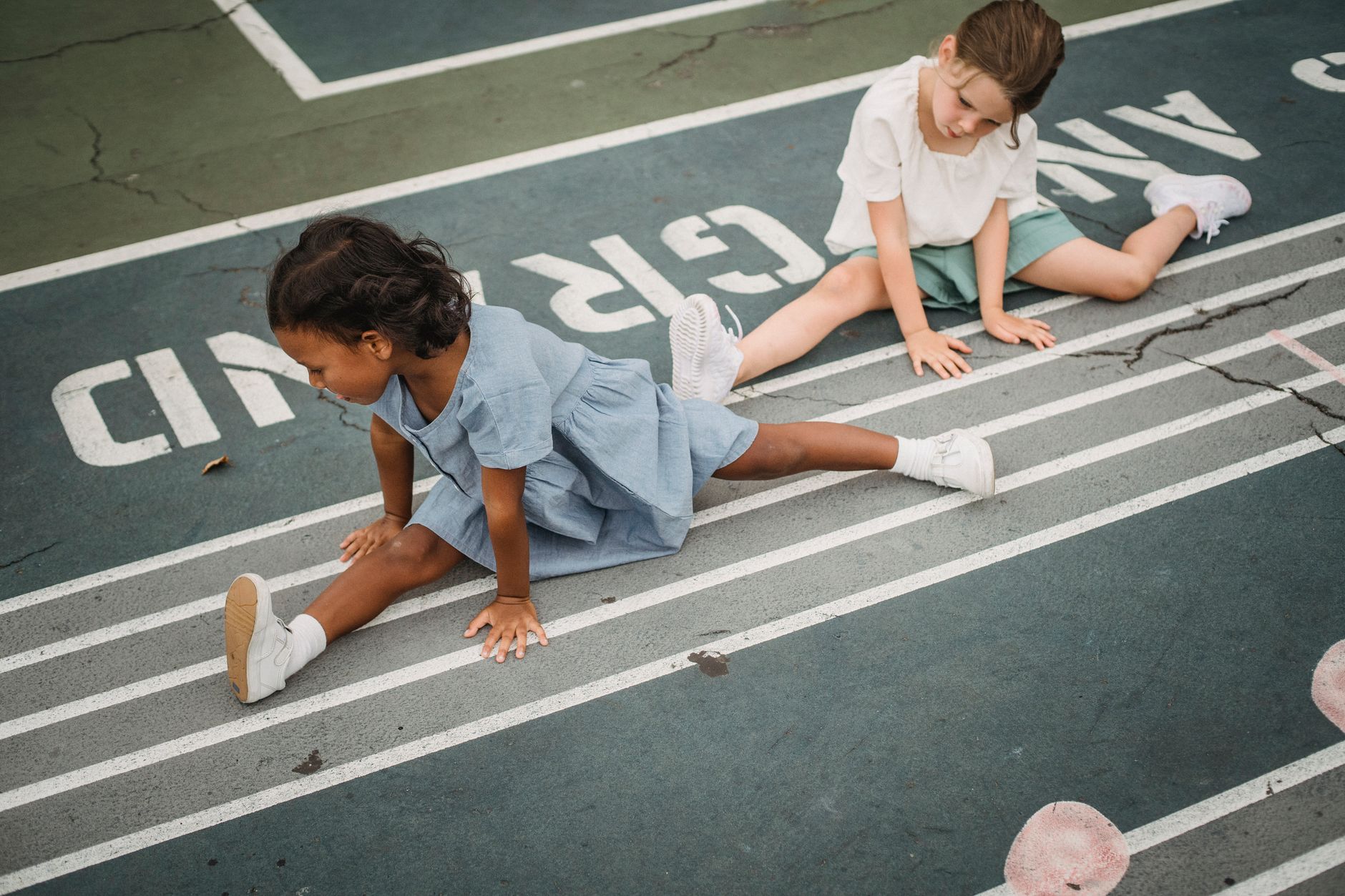 Two young girls stretch on a track, promoting fitness and flexibility.
