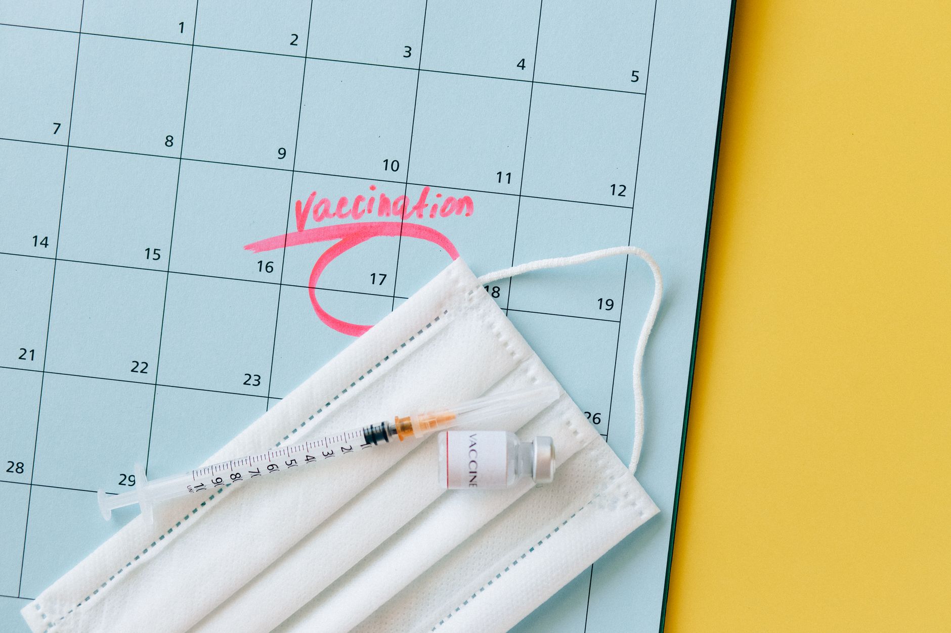 Close-up of a calendar marked for vaccination, with a syringe and face mask highlighting healthcare theme.