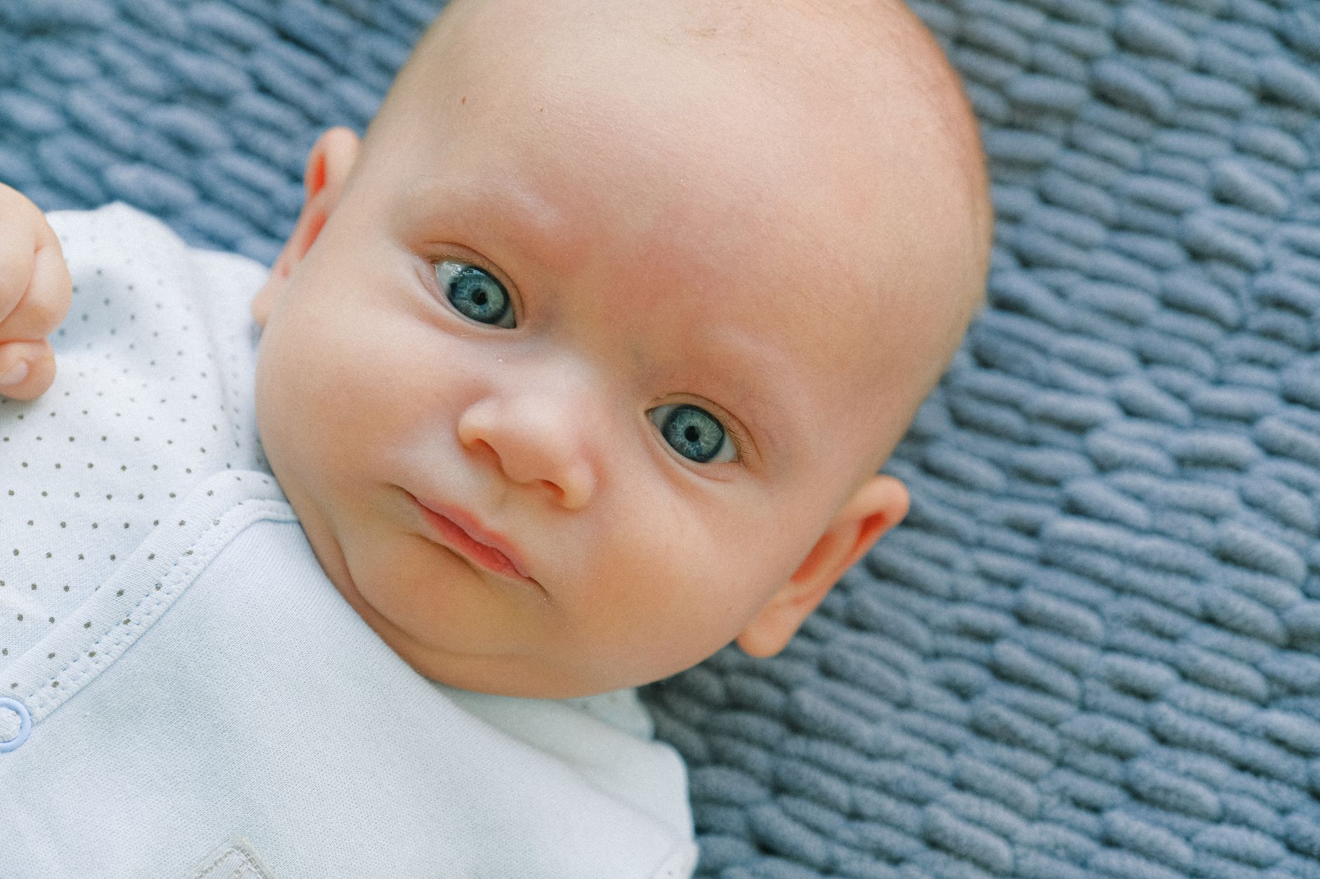 Close-up portrait of a cute baby with blue eyes lying on a soft textured blanket.