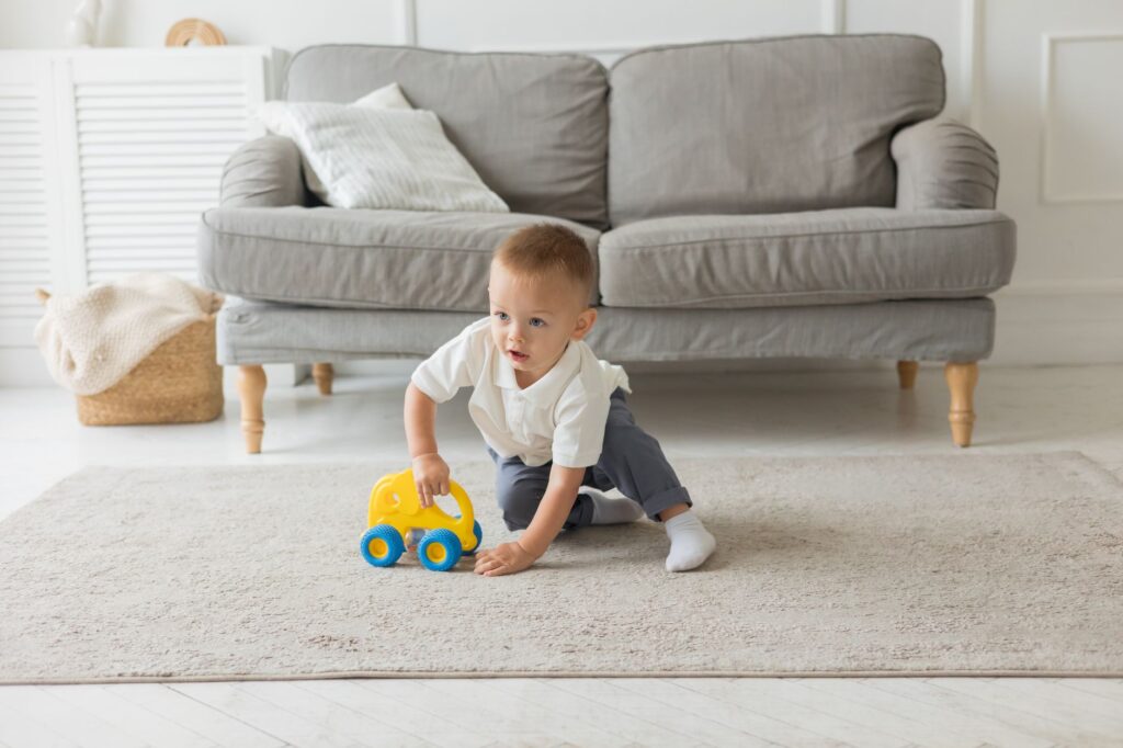 A young boy plays with a yellow toy car on the carpet in a cozy living room.