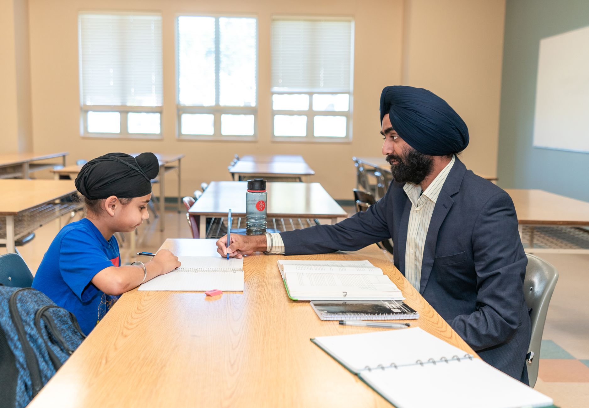 Male teacher helping a young student with studies in a classroom environment.