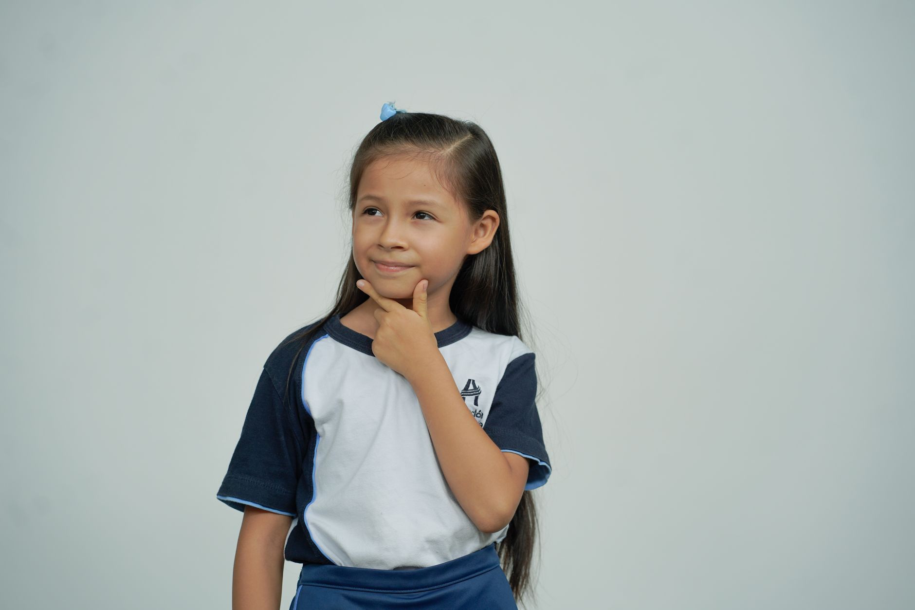 A young schoolgirl in uniform stands thoughtfully against a white background.