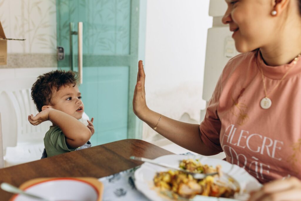 Mother and child enjoying a meal together, bonding through a high-five moment.