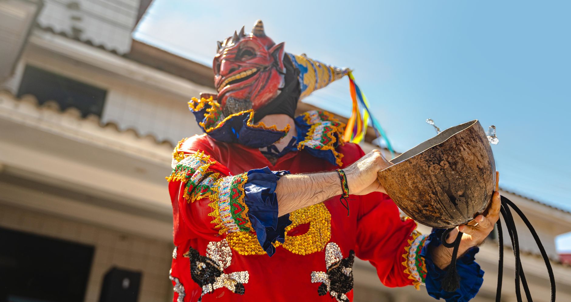 Colorful masked performer at a traditional festival in Rioja, San Martín, Peru, holding a ceremonial bowl.