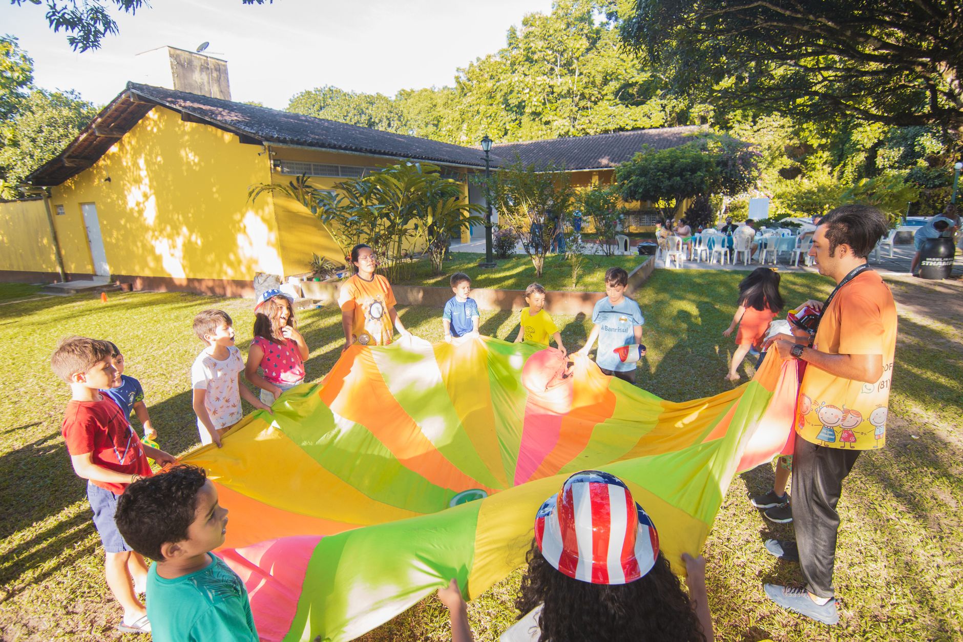 A joyful outdoor birthday party with children playing with a colorful parachute in a garden setting.
