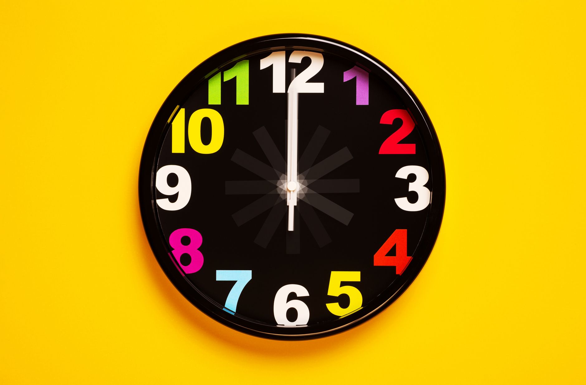 Vibrant wall clock with colorful numbers on a bright yellow background, emphasizing modern decor.