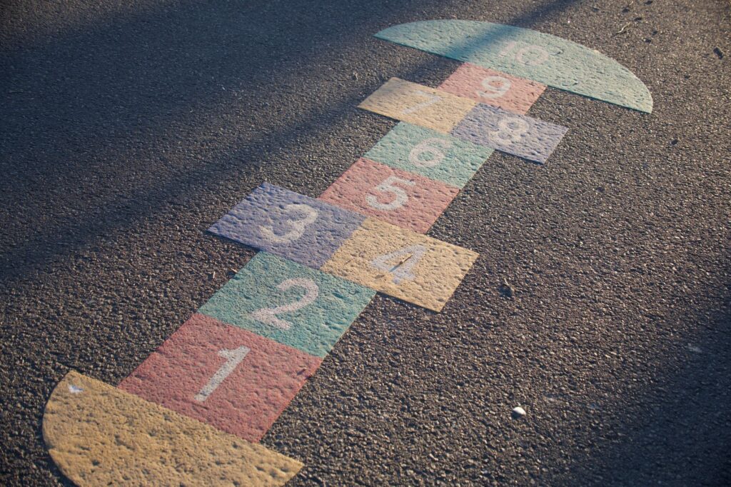 A vibrant hopscotch grid painted on an outdoor playground surface, lit by daylight.