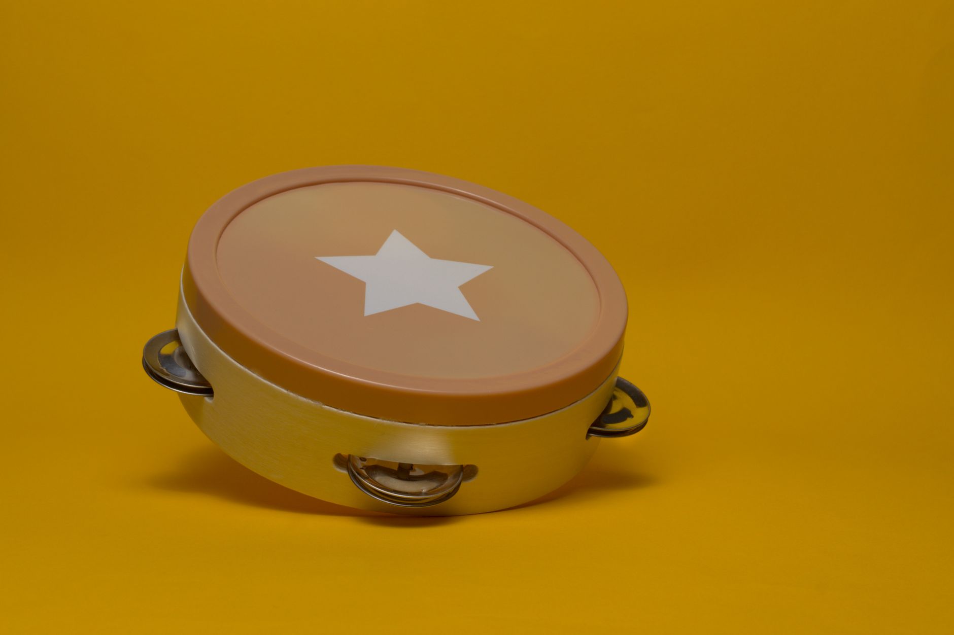Vibrant tambourine featuring a star design sits against a bold yellow backdrop, perfect for music-themed designs.