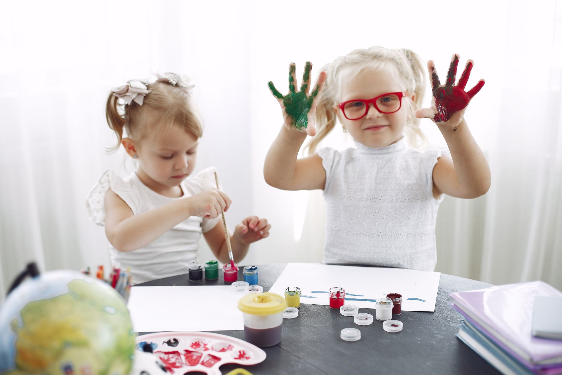 Small girls with braids in white tee shirts have drawing class in kindergarten