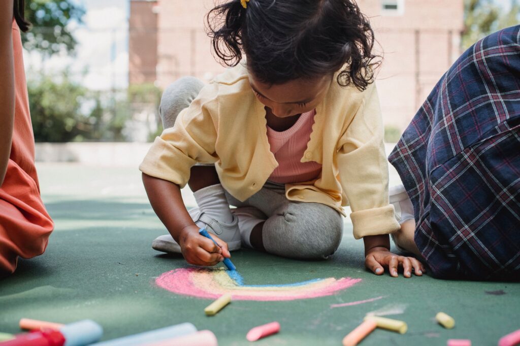 A young child enjoying creative play with chalk on a sunny outdoor playground.