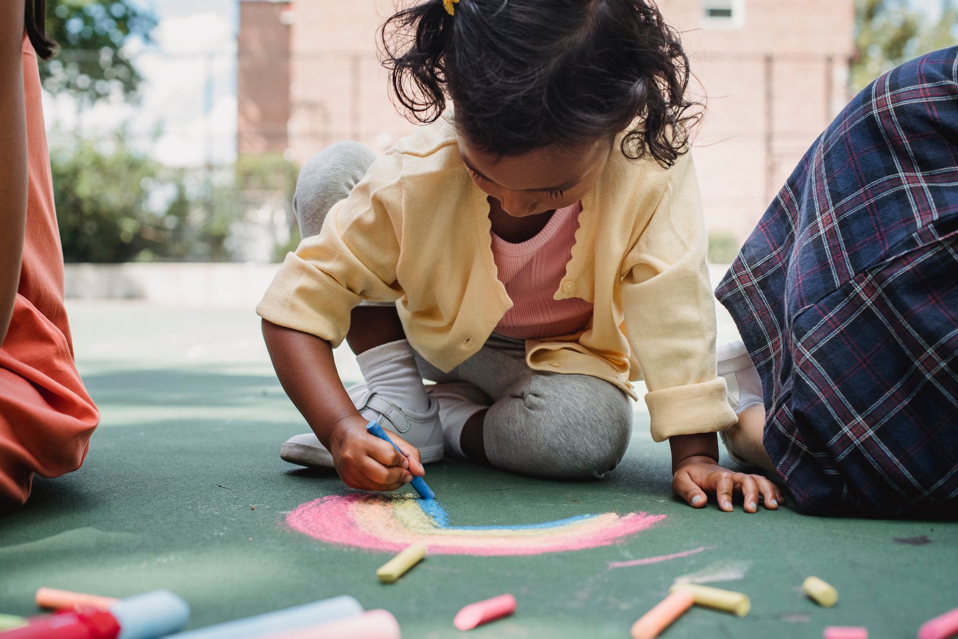 A young child enjoying creative play with chalk on a sunny outdoor playground.