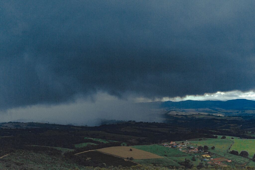 Aerial photograph showcasing sprawling fields and distant mountains beneath ominous rain clouds.