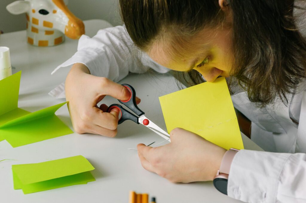 A young woman focuses on cutting colorful paper pieces for art and crafts at a table.