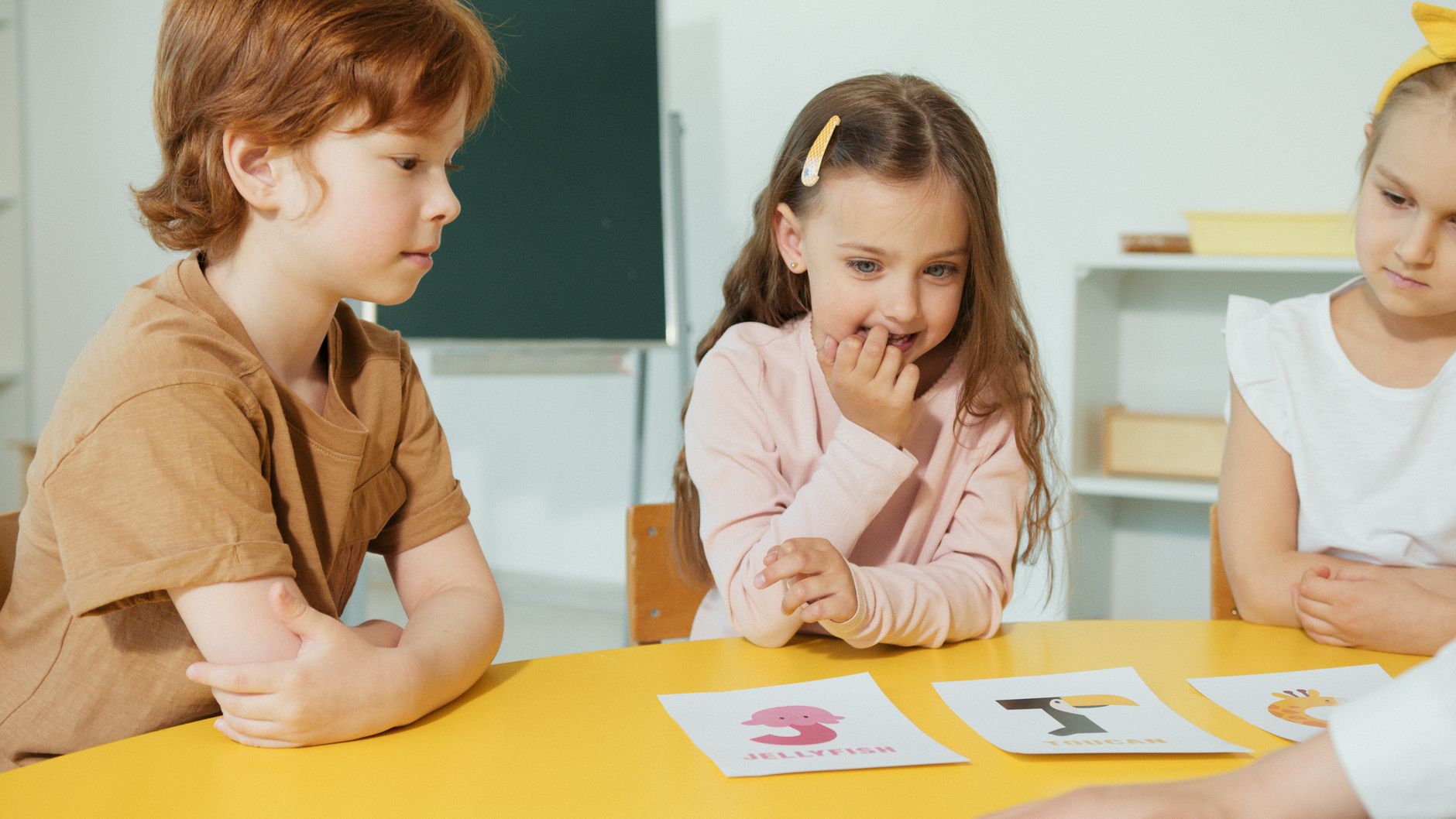 Group of kids engaging in a classroom activity with educational cards on a yellow table.