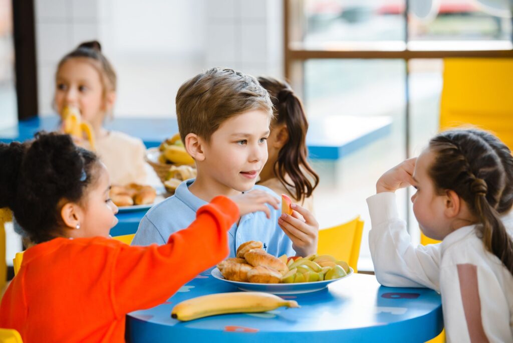 Group of diverse children enjoying a meal together indoors, fostering friendship and sharing.
