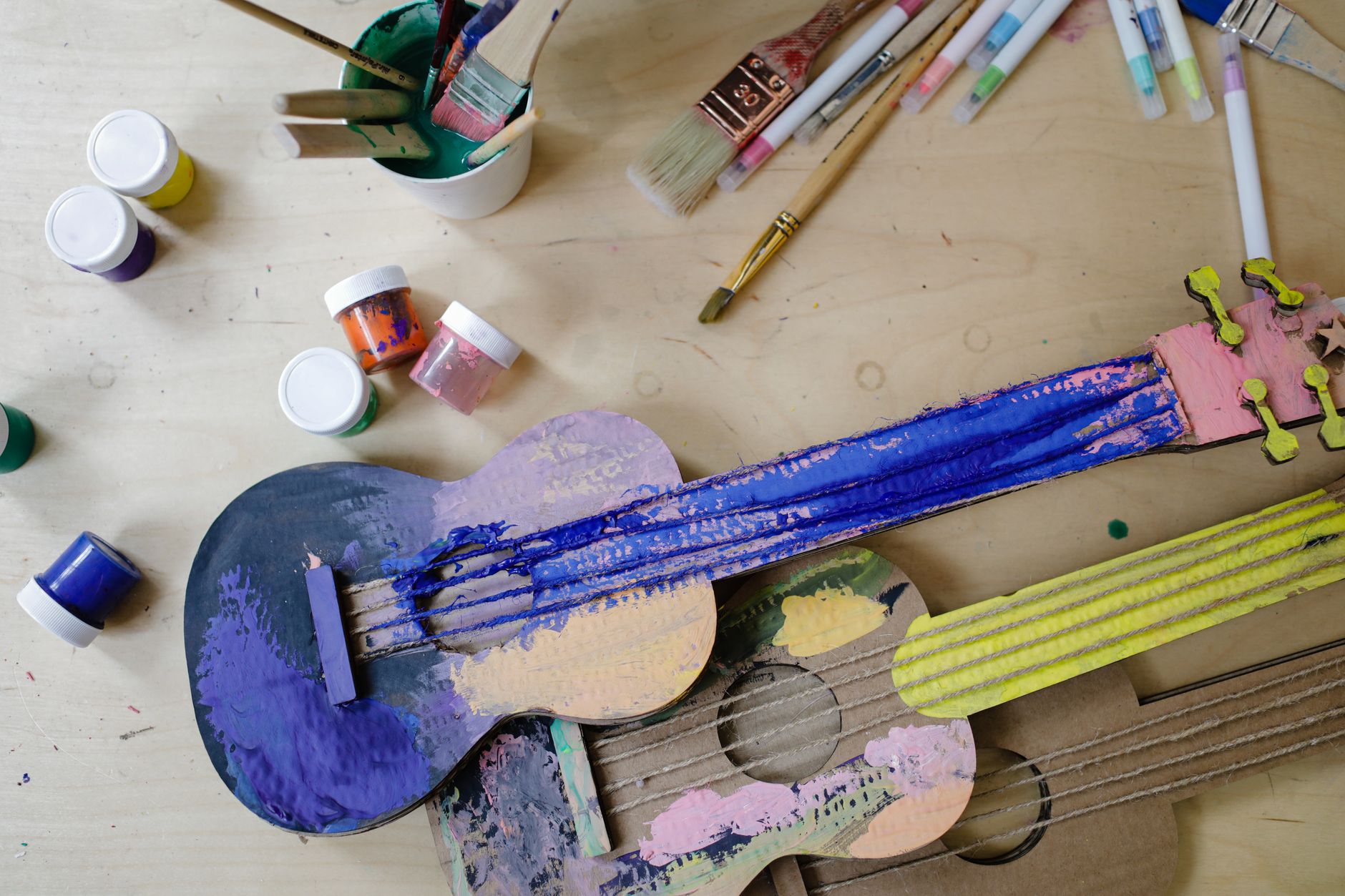 Colorful cardboard guitars with paints and brushes, showcasing artistic creativity.