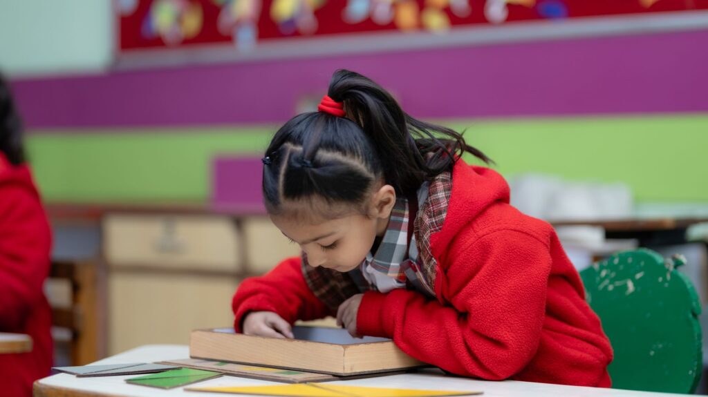 A young girl engrossed in a creative activity at a colorful classroom desk.