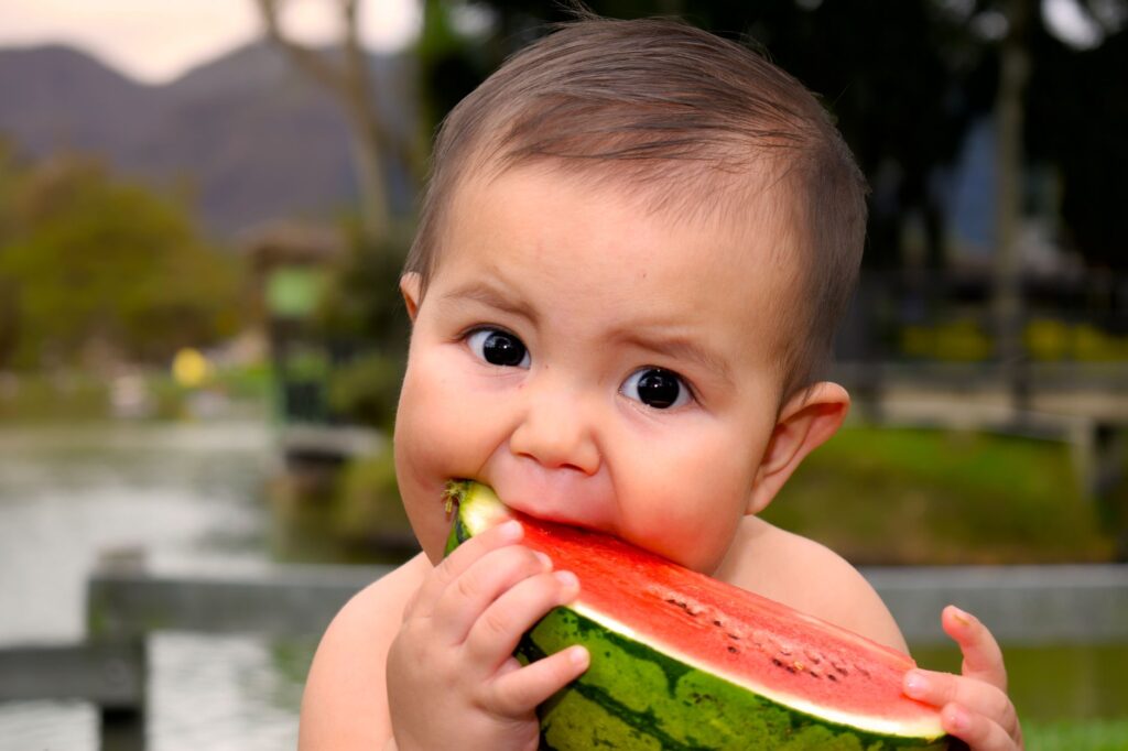 Cute baby eating a juicy watermelon slice outdoors in a park setting.
