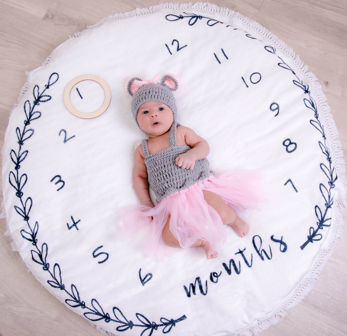 Cute baby photographed on a milestone blanket wearing a knit outfit and pink tutu, showcasing a month marker.