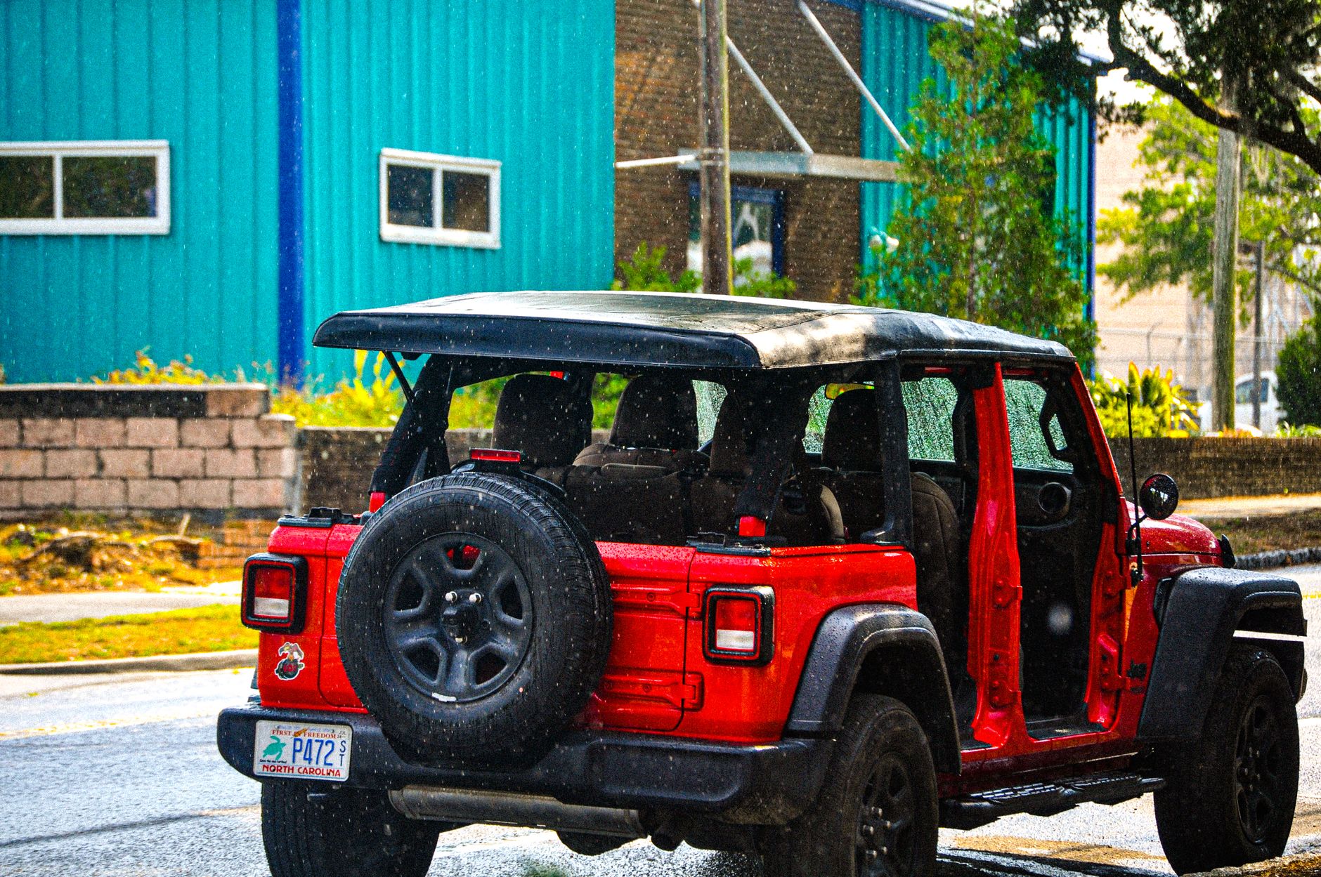 Back view of a red Jeep Wrangler driving on a rainy city street, showcasing urban life and adventure.