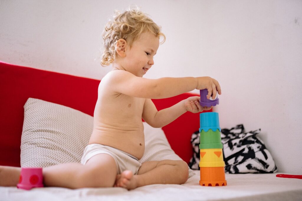 A cheerful toddler building a tower with colorful plastic stacking toys on a sofa.