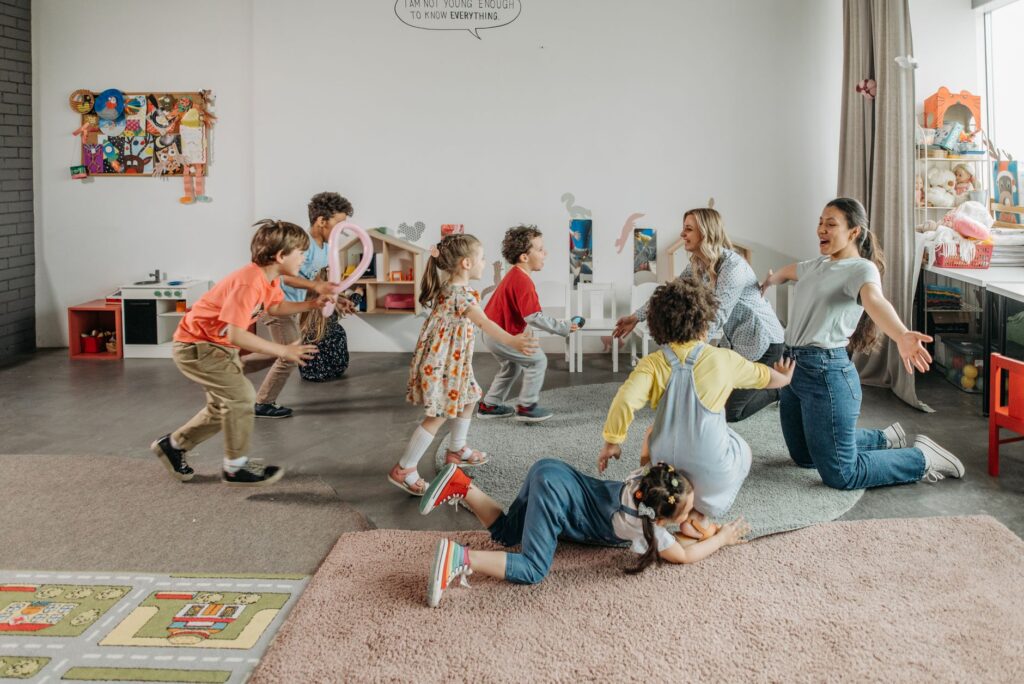 Joyful children and teachers playing together in a colorful classroom setting.